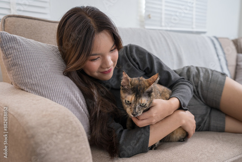 A woman lying on a couch, lovingly cuddling with her tortoiseshell cat. The intimate moment reflects the strong bond and comfort