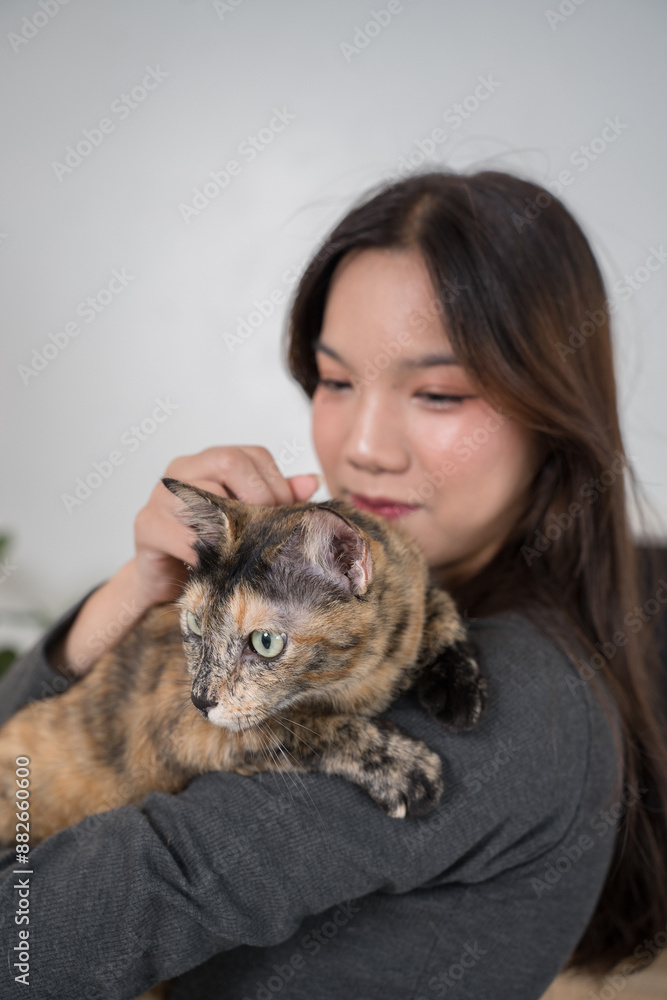A woman standing in a living room, holding her tortoiseshell cat close to her chest. The setting is calm and domestic A woman standing in a living room, holding her tortoiseshell cat close to her chest. The setting is calm and domestic