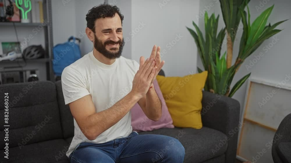 Happy middle age man clapping with joy at home, smiling and applauding in white t-shirt indoors