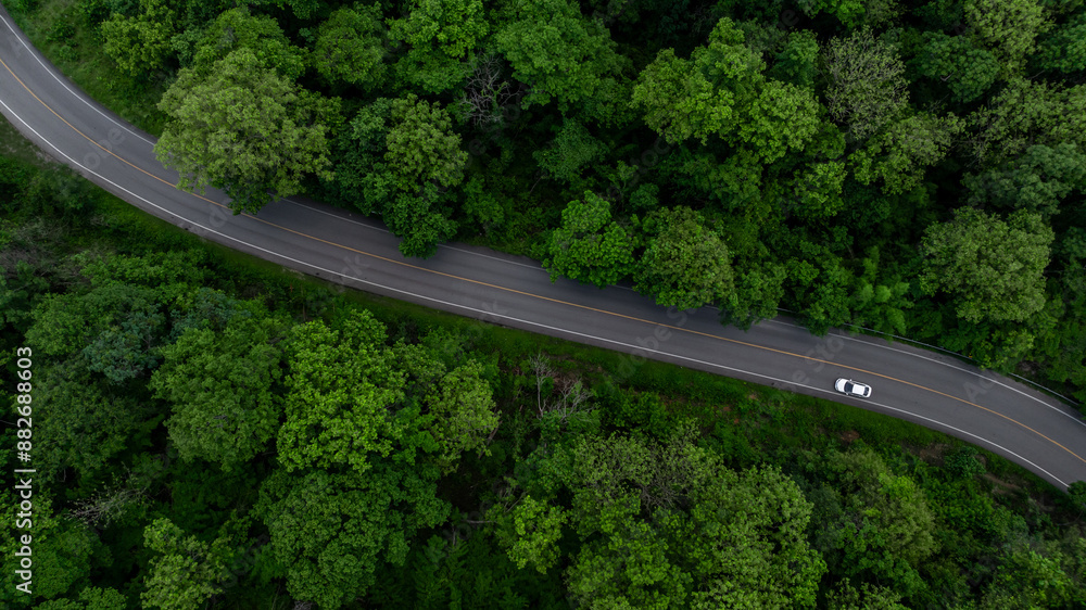Aerial view electric vehicle car driving on asphalt road in mountain green forest, EV car electric vehicle car on forest road green energy and eco power, White electric car driving green forest road.