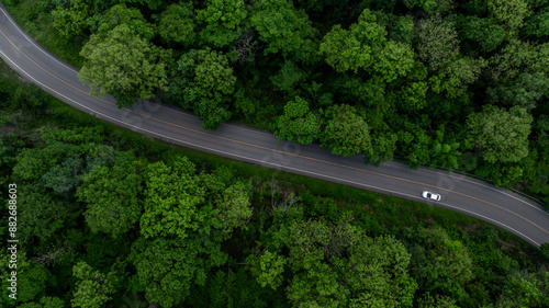 Obraz na płótnie Aerial view electric vehicle car driving on asphalt road in mountain green forest, EV car electric vehicle car on forest road green energy and eco power, White electric car driving green forest road. w salonie