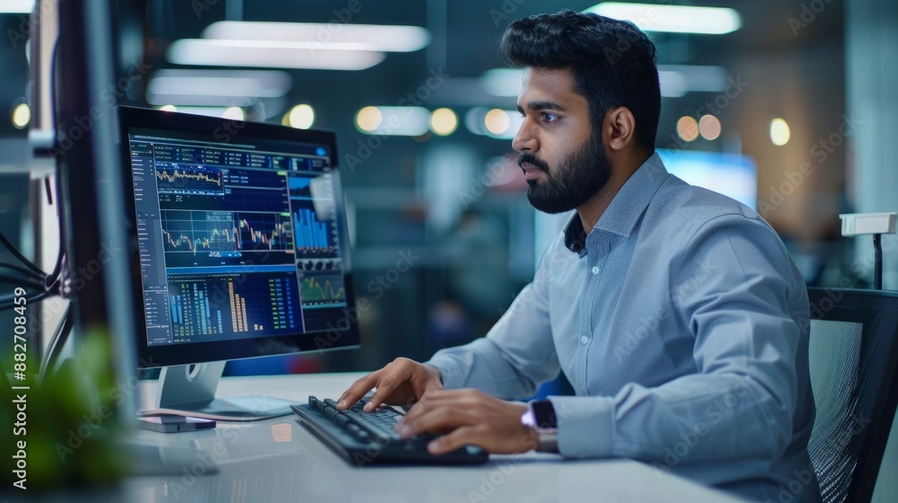 Portrait of a South Asian financial securities trader working on a desktop computer in a modern office. The financial elite in a modern office Portrait of a South Asian financial securities trader working on a desktop computer in a modern office. The financial elite in a modern office