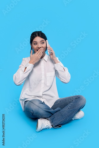 Surprised Woman Talking on Phone Sitting on Blue Background