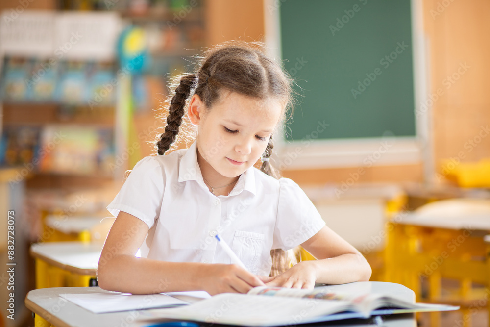 A cute girl sits in a classroom at a desk during a lesson. The child is in first grade. The girl learns lessons. Back to school. School supplies on the desk.
A cute girl sits in a classroom at a desk during a lesson. The child is in first grade. The girl learns lessons. Back to school. School supplies on the desk.