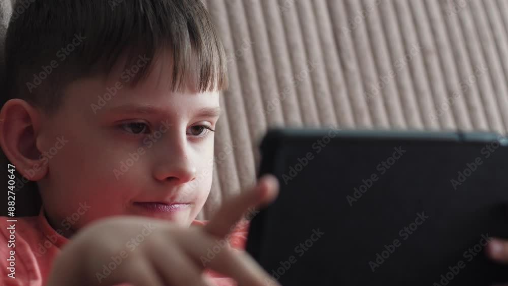 Caucasian boy 9-10 years old uses a tablet computer while sitting on the sofa at home. teenager uses a gadget Caucasian boy 9-10 years old uses a tablet computer while sitting on the sofa at home. teenager uses a gadget