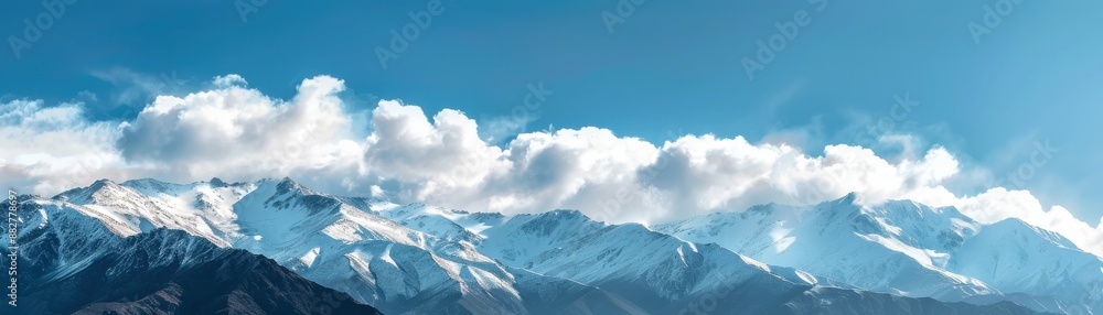 Panoramic view of snowy mountain peaks under a clear blue sky with fluffy clouds. Panoramic view of snowy mountain peaks under a clear blue sky with fluffy clouds.