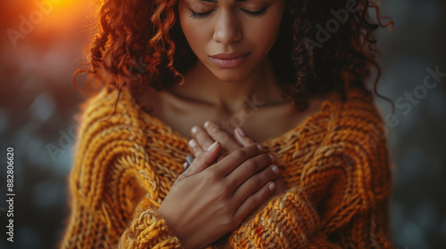 Curly-haired woman embracing herself in orange sweater, eyes closed in peaceful introspection. Concept of self-love, mindfulness, and inner peace.