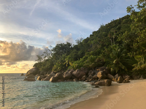 Tranquil beach with golden sand, turquoise water, and lush tropical vegetation on Praslin island in Seychelles