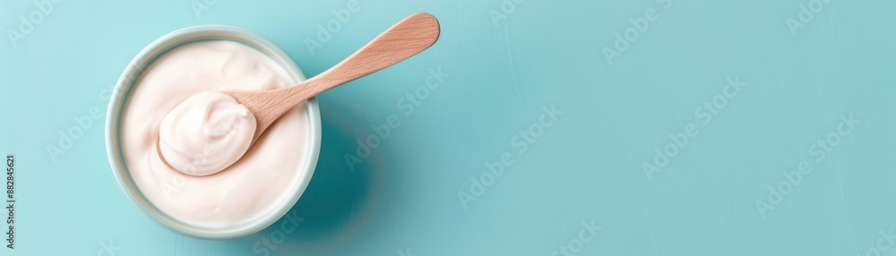 A bowl of creamy yogurt with a wooden spoon against a light blue background. Perfect for illustrating healthy eating and breakfast concepts. A bowl of creamy yogurt with a wooden spoon against a light blue background. Perfect for illustrating healthy eating and breakfast concepts.