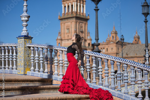 Young, beautiful, brunette woman in black shirt and red skirt, dancing flamenco on the stairs of a beautiful bridge in Spain square in Seville. Flamenco concept, dance, art, typical Spanish.