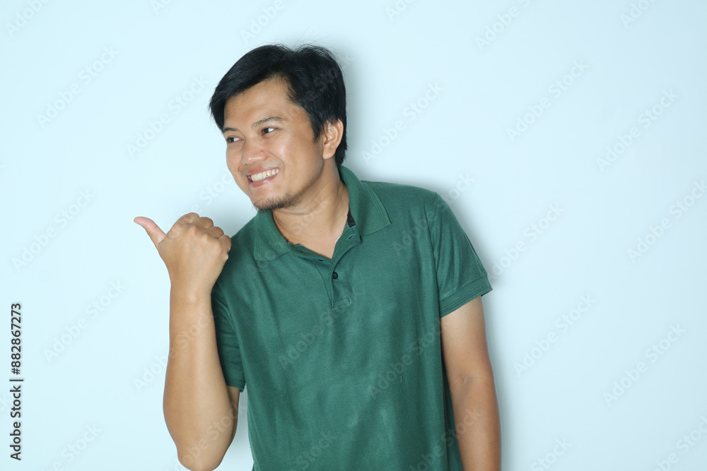 Young Asian man smiles and pointing to the right side with his thumb. Wearing a green t-shirt