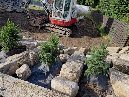 preparing a garden in the mountains. excavation work and landscaping with the planting of spruce trees between granite boulders