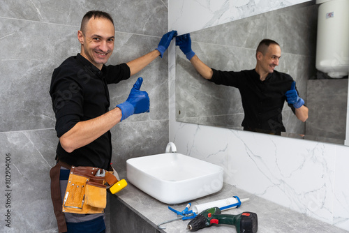 The worker installs the mirror in the bathroom.