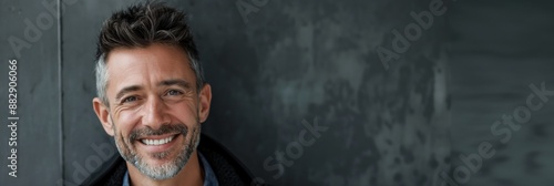 A handsome, smiling man with a beard poses confidently in a studio portrait, exuding a blend of masculinity and modern style.