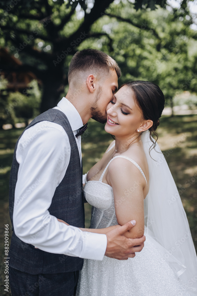 Beautiful young happy smiling groom in a gray suit and bride in a white dress hugging and kissing outdoors in the park. Wedding photography close-up, portrait of stylish newlyweds. Beautiful young happy smiling groom in a gray suit and bride in a white dress hugging and kissing outdoors in the park. Wedding photography close-up, portrait of stylish newlyweds.