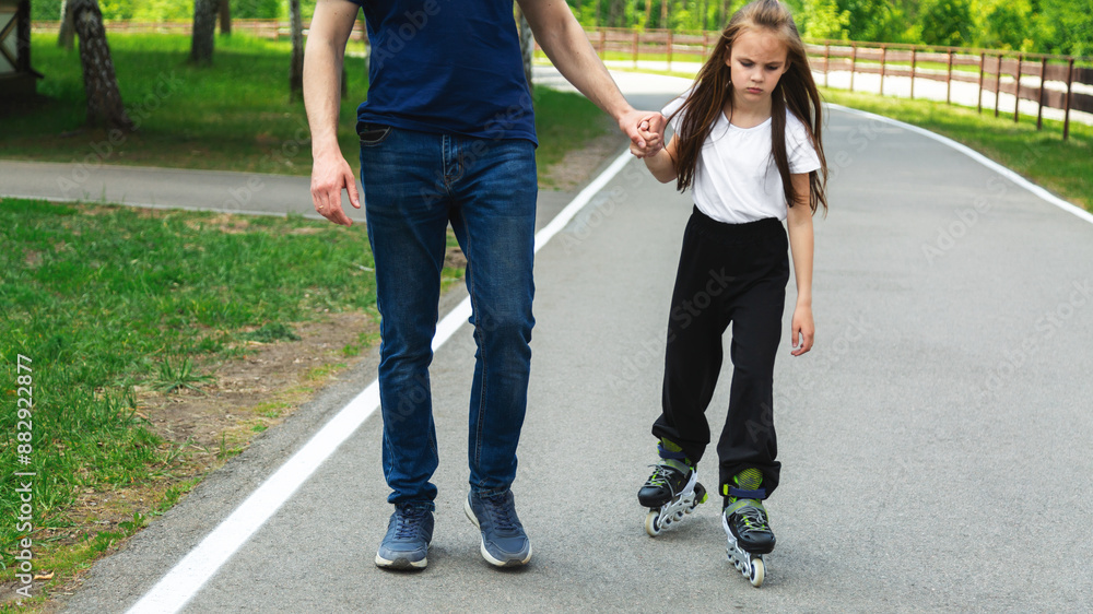 Obraz premium Skating, learning and father holding hands of his child while teaching her on the park. Family, love and dad helping his young girl kid for support, balance and care to outdoor roller skate