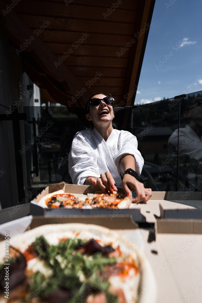 A woman in a bathrobe eats pizza on a balcony overlooking the mountains. Hotel holiday concept. Pizza A woman in a bathrobe eats pizza on a balcony overlooking the mountains. Hotel holiday concept. Pizza