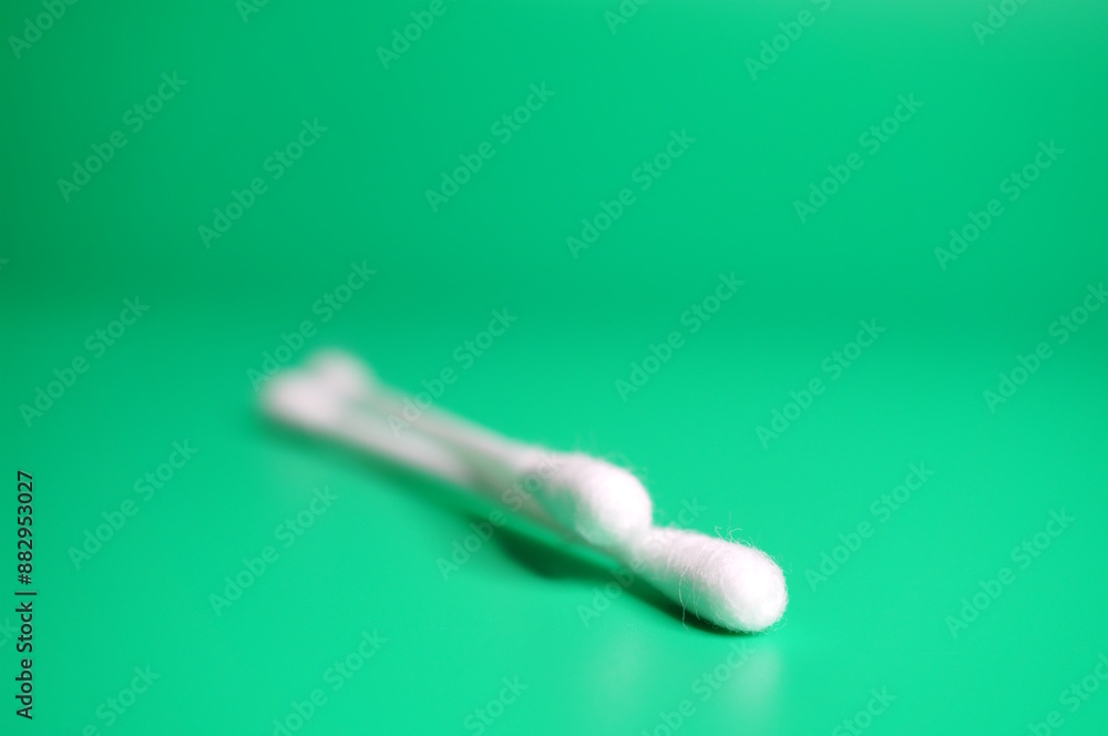 A cotton swab for ears on a green background. Body care and hygiene. A cotton swab for ears on a green background. Body care and hygiene.