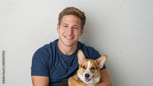 A man in a blue shirt holds his corgi dog close in a loving embrace. The man is smiling and looking down at his dog. The dog is looking up at the man with a happy expression