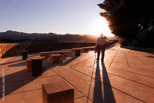 Old man with a walking stick watching a sunset with mountains in the background (Ronda, Malaga)