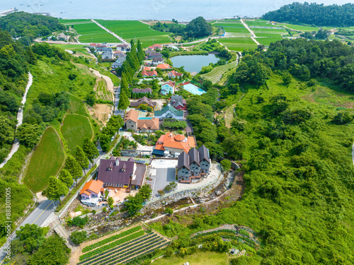 Yongso-ri, Namhae-gun, Gyeongsangnam-do, South Korea - June 17, 2023: Aerial and summer view of road and houses with trees against rice paddy near the eaa at American Village
 photo