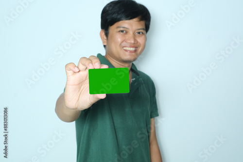 Young Asian man smiles while showing green card with selective focus. Wearing a green t-shirt photo