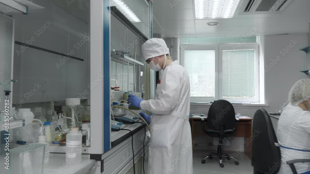 Multiple Medical Workers operating in the Medical Laboratory. A Male laborant shakes the Plastic Container with Liquid Substance. Slowly Pouring the Fluid into the Beaker. Medical Production Process. Multiple Medical Workers operating in the Medical Laboratory. A Male laborant shakes the Plastic Container with Liquid Substance. Slowly Pouring the Fluid into the Beaker. Medical Production Process.