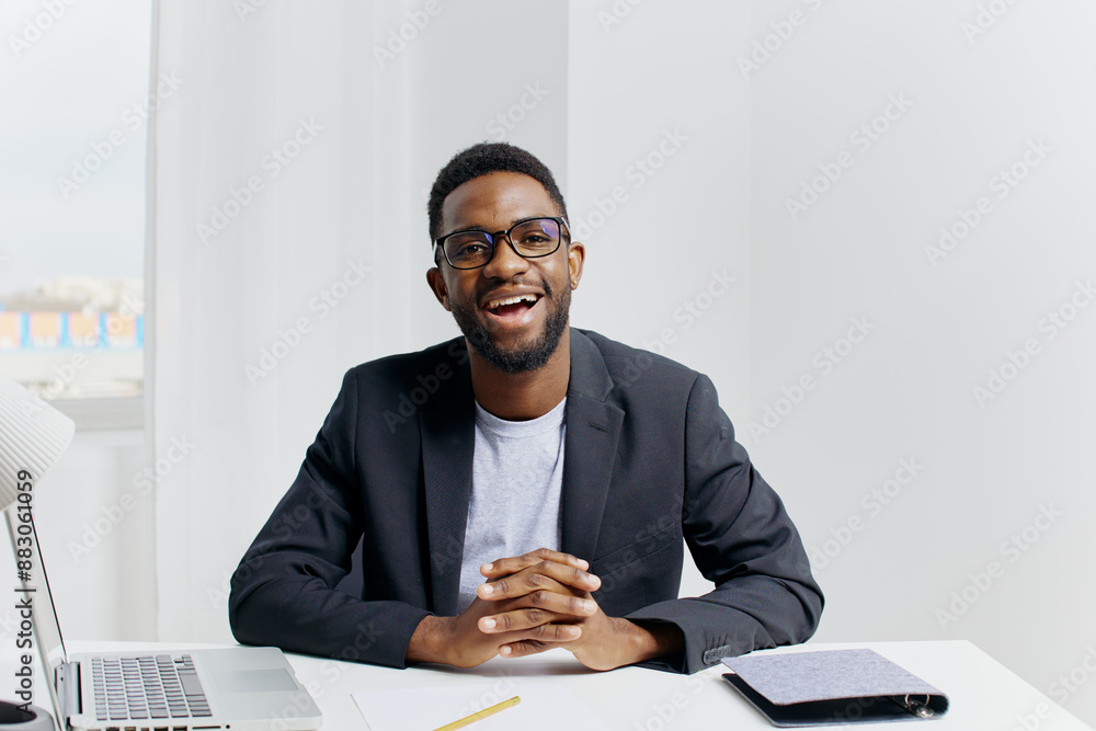 Confident businessman in a suit working on a laptop at his desk, smiling and holding a pen Confident businessman in a suit working on a laptop at his desk, smiling and holding a pen
