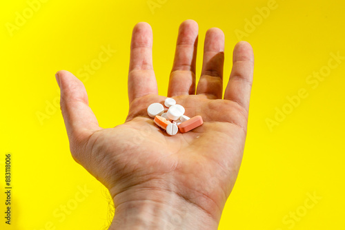 Hand Holding Assortment of Pills Against Yellow Background