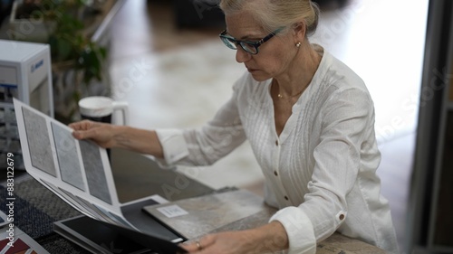 Happy mature woman looking at samples of floor tiles in a store, consider using vct, lvp, or engineered tile in a home renovation redecorating project. photo