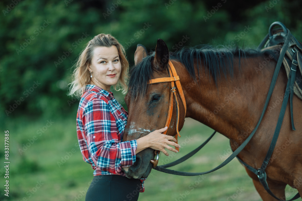 Obraz premium Happy blonde with horse in forest. Woman and a horse walking through the field during the day. Dressed in a plaid shirt and black leggings.