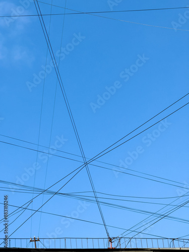 Close-up shot of tangled electrical wires intersecting against a bright blue sky, illustrating urban infrastructure and connectivity. photo