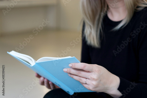 Close up portrait of a woman sitting on a couch and holding a blue mockup book. Education, reading and studying concept 