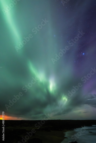 Long exposure of the Aurora Borealis above a beach in the Icelandic Westfjords with a starry sky.