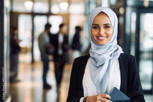 smiling young entrepreneur wearing headscarf holding diary while standing in office