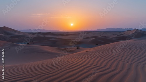 The setting sun casts a warm glow over rippled sand dunes in the expansive Saudi desert.