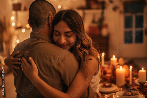 Hispanic couple embracing in warmly lit dining room with candles and festive decorations, celebrating Thanksgiving. The cozy atmosphere emphasizes love and togetherness, creating a romantic holiday sc © MarGa