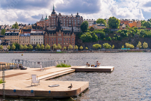 People enjoying the summer sun on a sand bed infront of historical buildings of Södermalm, from the island of Riddarholmen, near Lake Mälaren. Stockholm, Sweden photo