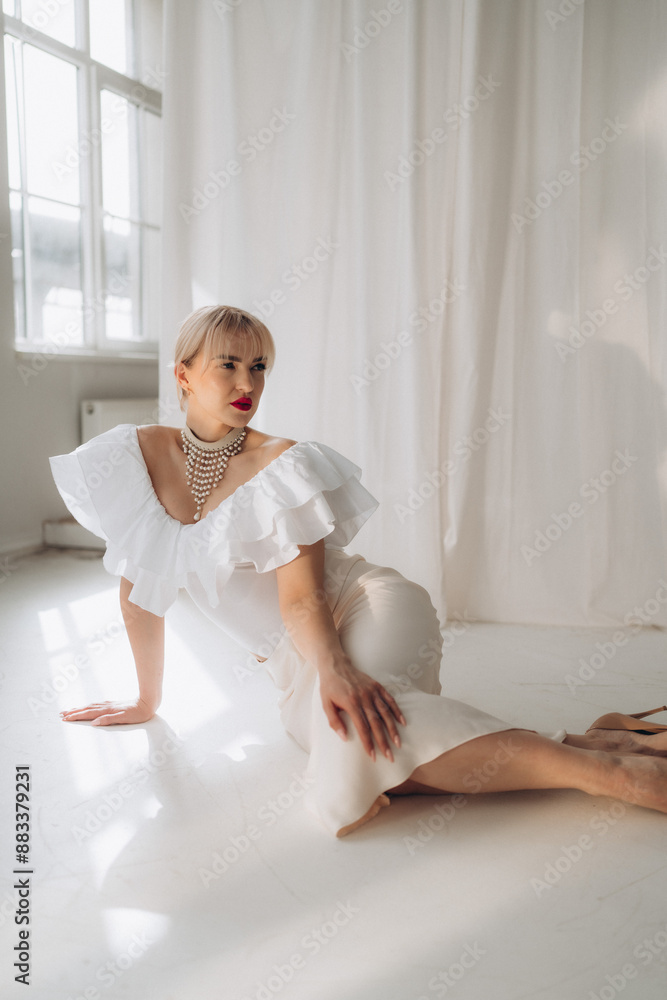 Elegant woman with blonde bob haircut and red lipstick posing on all fours in a white ruffled dress and pearl necklace, against a white background. Copy space. Elegant woman with blonde bob haircut and red lipstick posing on all fours in a white ruffled dress and pearl necklace, against a white background. Copy space.