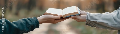 Two hands exchanging an open book in an outdoor setting, symbolizing the sharing of knowledge and information in a natural environment.