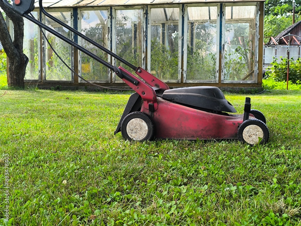Fototapeta premium The electric mower stands on the green grass. preparation for mowing the lawn. 