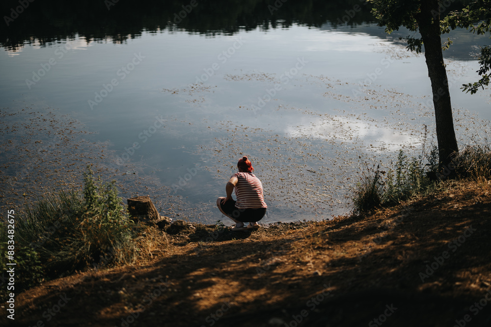 Fototapeta premium Individual crouching by a serene lake, encapsulating the essence of solitude and relaxation in nature