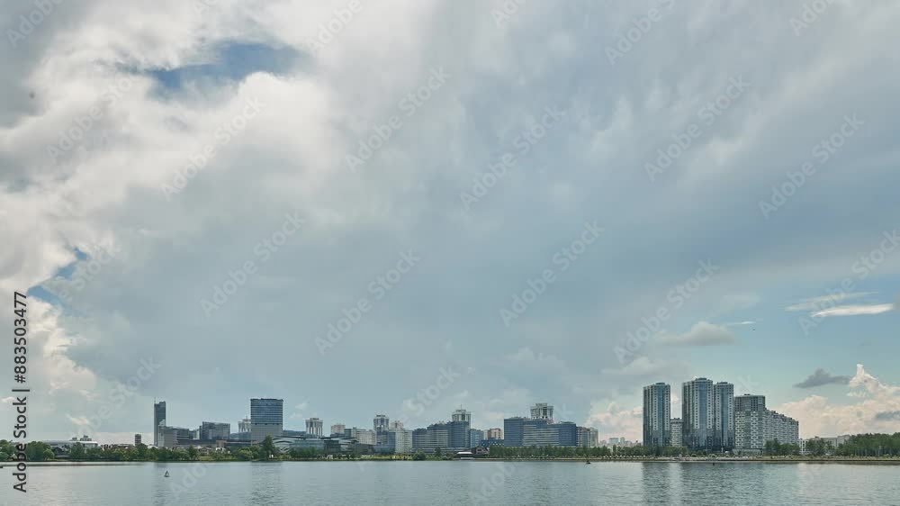 A city on the shore of a lake. Timelapse clouds float over skyscrapers. The houses of a modern city by the water against the sky. A city on the shore of a lake. Timelapse clouds float over skyscrapers. The houses of a modern city by the water against the sky.