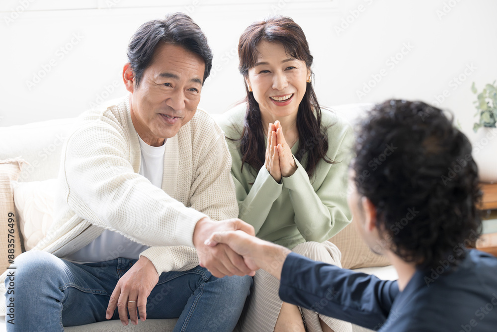 営業マンの説明を受ける笑顔の50代夫婦　投資や保険、不動産など　契約成立の握手と拍手で喜ぶ妻