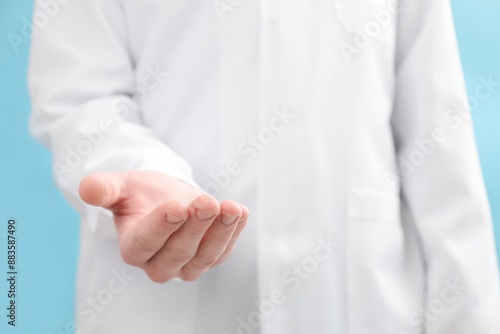Doctor holding something on light blue background, selective focus