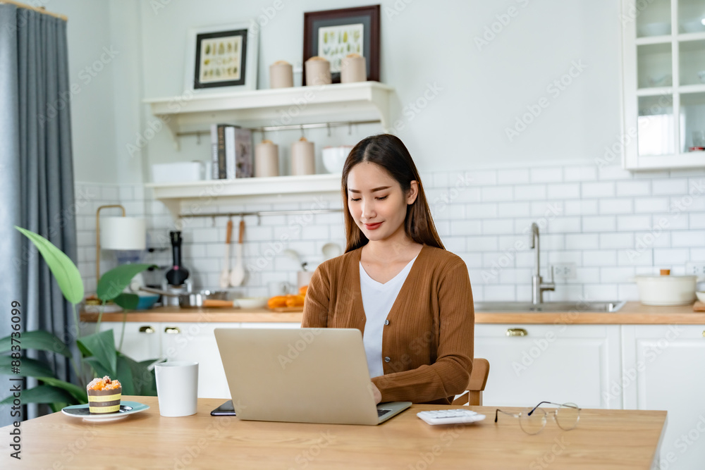 Beautiful young Asian woman working with laptop computer in home kitchen. Work at home Beautiful young Asian woman working with laptop computer in home kitchen. Work at home