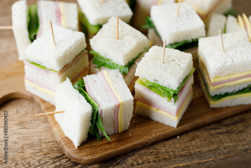 Sandwich of white soft bread with ham, cheese and lettuce on wooden board.