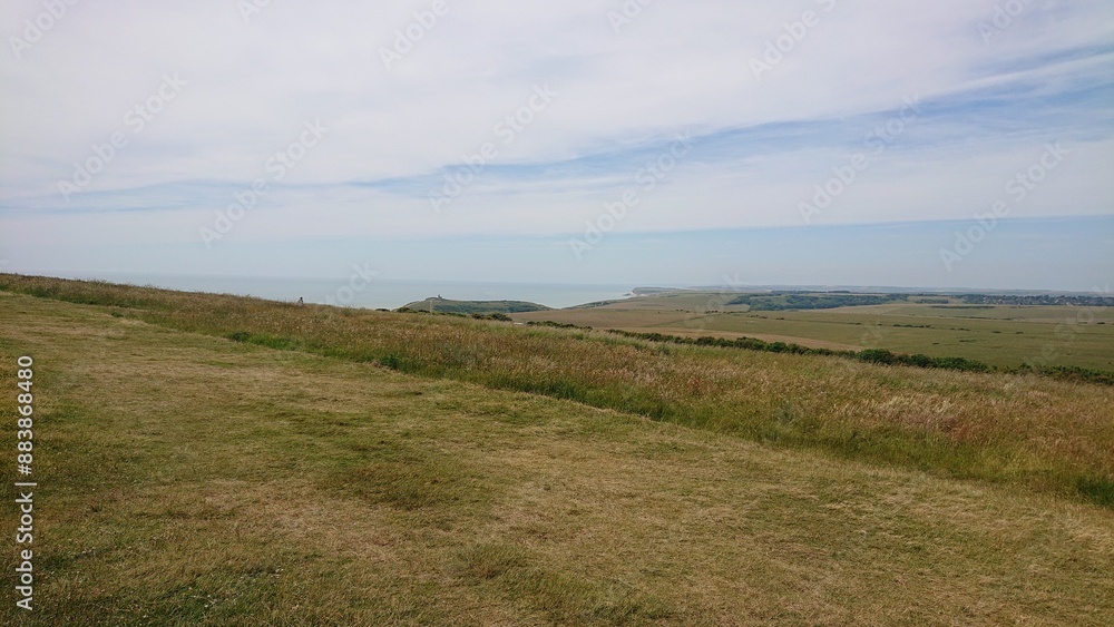 A tranquil landscape of rolling grassy hills meeting the sea, with expansive views and a lighthouse in the distance. A tranquil landscape of rolling grassy hills meeting the sea, with expansive views and a lighthouse in the distance.
