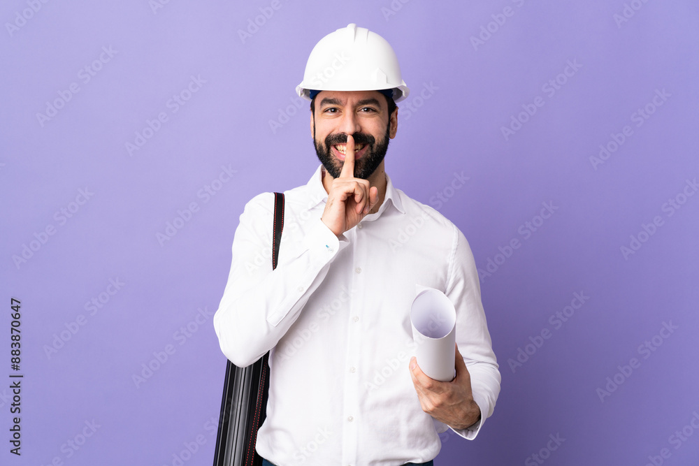 Young architect man with helmet and holding blueprints over isolated purple background showing a sign of silence gesture putting finger in mouth Young architect man with helmet and holding blueprints over isolated purple background showing a sign of silence gesture putting finger in mouth