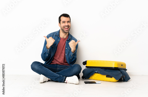 Caucasian handsome man with a suitcase full of clothes sitting on the floor at indoors with thumbs up gesture and smiling